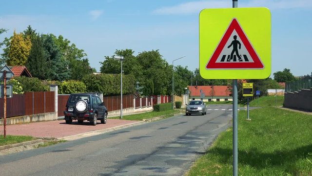 Warning traffic sign Crosswalk in village with passing cars in sunny summer day 