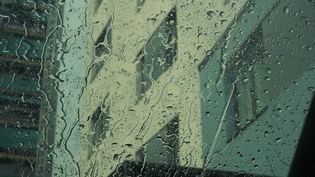 Rain drops fall on the windscreen of a car - building in the background