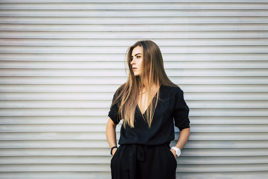 trendy beautiful woman in black jumpsuit watching to the left relaxing in harmony on the white roller wall background