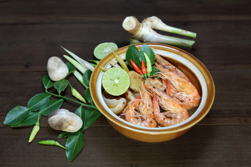 Tom Yum Kung Shrimp clear soup  is decorated with lime, red pepper, lemongrass, galangal, kaffir lime leaf, chilli paste and mushroom on wooden background, Hot and spicy food, Thai food.