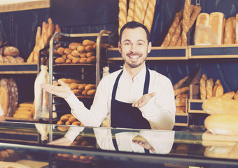 Positive male seller showing assortment of bakery