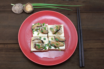 Steamed tofu with Minced pork and mushroom, topping with black pepper and green leaf onion in red dish on wooden background, Chinese food.
