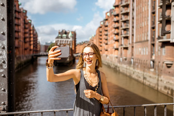 Young woman tourist making selfie photo on the beautiful water channel background in Speicherstadt,...