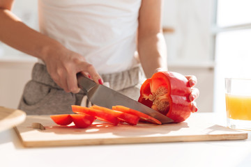 Obraz na płótnie Canvas Close up portrait of young woman slicing red capsicum