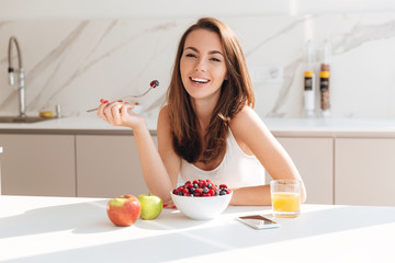 Smiling young woman eating fresh berries from a bowl - Powered by Adobe
