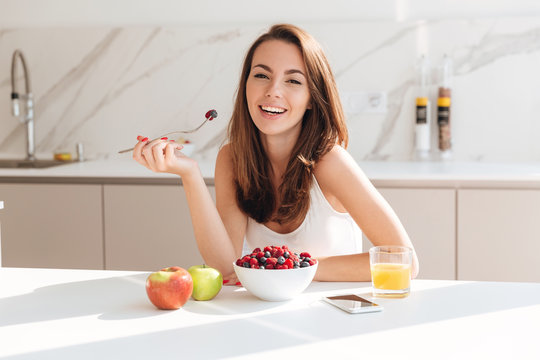 Smiling young woman eating fresh berries from a bowl