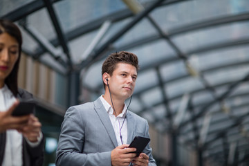 Businessman listening to podcast waiting for train at station