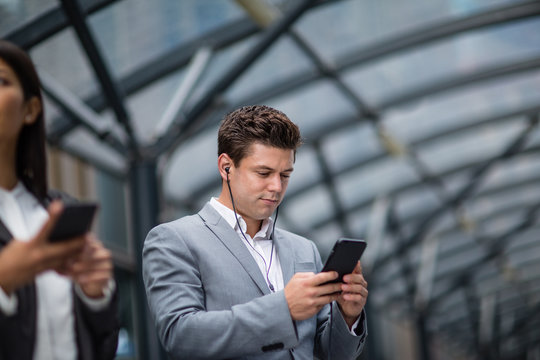 Businessman listening to podcast waiting for train at station