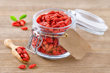 organic goji berries in a glass jar with label for text on wooden background