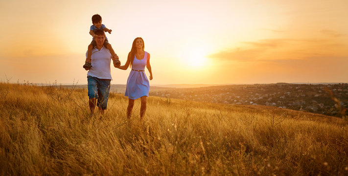 Happy family walking on field in nature at sunset.