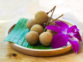 Tropical sweet fruit, Longan with fresh green  banana leaf and purple orchid on wooden dish with wooden table background