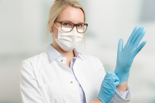 Junge hübsche Ärztin mit Mundschutz zieht Handschuhe an