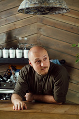 Young friendly bartender with mustache and beard standing at the bar counter in loft-styled cafe. Former factory building, natural daylight.