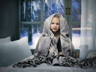 small child wrapped in a blanket on the bed. Children's room window. Outside the window, snow,...