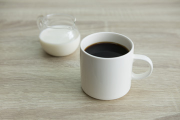 WHITE COFFEE CUP WITH MILK JAR
White coffee cup with transparent milk jar on the wood table. 
