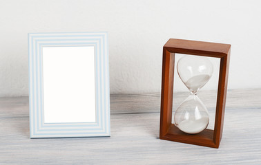 Photo frames next to hourglass on wooden table. Decor.