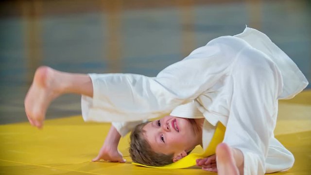 Students are doing a backward somersault on a yellow mat. They are having a judo practise.
