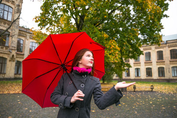 Happy woman walking in autumn city park. Rainy weather and yellow trees around