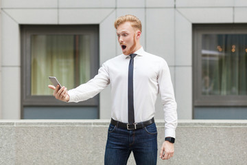 Ginger young adult business person looking at screen smart phone with shocked face.