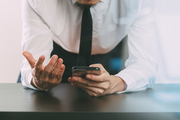 close up of businessman working with smart phone on wooden desk in modern office