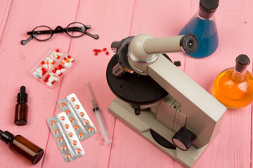 Workplace scientist / doctor - microscope, pills, syringe, eyeglasses, chemical flasks with liquid on pink wooden table