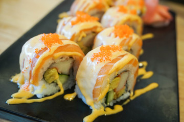 Sushi salmon roll with topped spicy sauce on black dish