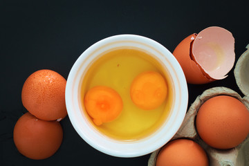 organic eggs and yolk broken in white cup on black background