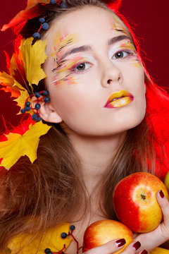 Beautiful young woman with autumn make up holding apples in her hands posing in studio over red background. Fashion concept.