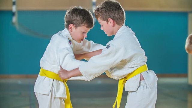Two boys with yellow belts are fighting. They are having judo practise in a school gym.