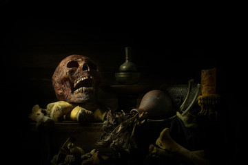 still life photography : human skulls, dry flower and candle on black table against art dark background with window light