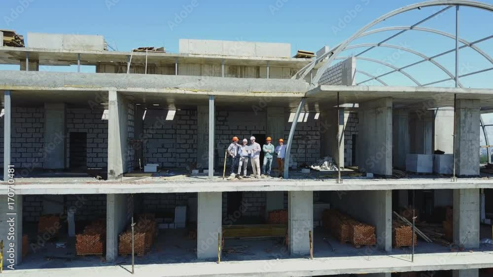 Poster aerial shot of builders team on construction site discussing plan of project with architect and cont