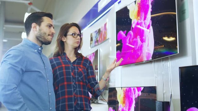 Young Couple Shopping for a New 4K TV Set in the Electronics Store. They're Trying to Decide on the Best Model But Have Doubts. Shot on RED EPIC-W 8K Helium Cinema Camera.