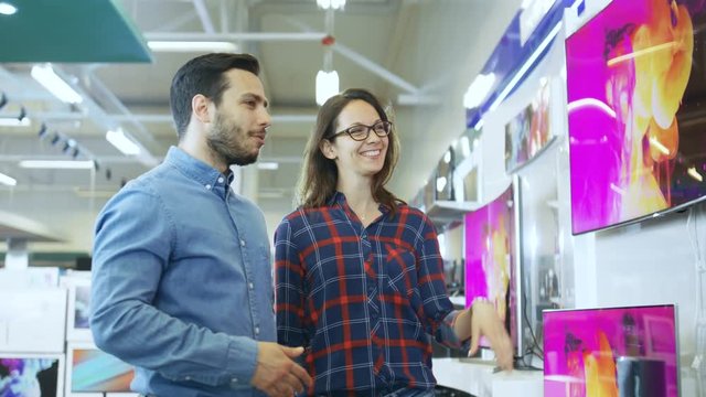 Young Couple Shopping for a New 4K TV Set in the Electronics Store. They're Trying to Decide on the Best Model But Have Doubts.Shot on RED EPIC-W 8K Helium Cinema Camera.
