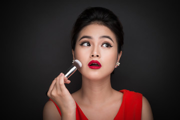 Fototapeta premium Cosmetic powder brush. Asian woman applying blusher on her cheeks with perfect make-up and red lips