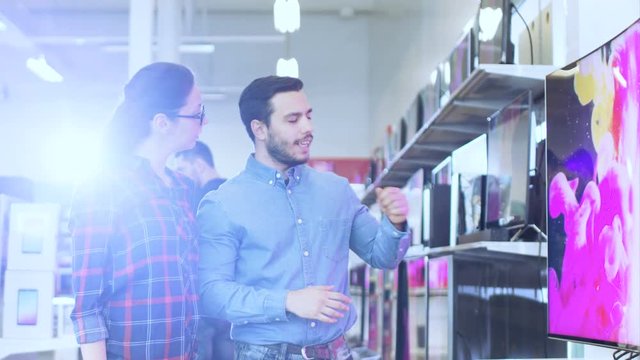Young Couple Shopping for a New 4K Television Set in the Electronics Store. They're Deciding on the Best Model for Their Happy Family House. Shot on RED EPIC-W 8K Helium Cinema Camera.