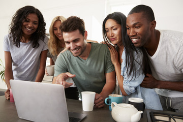 Friends Looking At Laptop And Drinking Coffee In Modern Kitchen