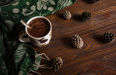 Cup of hot chocolate on rustic wooden bench, closeup photo of warm with mug and cones, winter morning concept