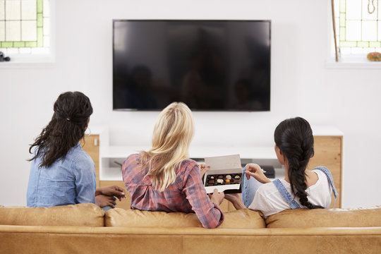 Female Friends Sitting On Sofa Watching Television Eating Candy