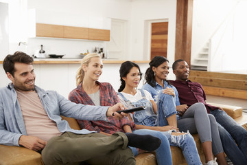 Group Of Friends Sitting On Sofa Watching Television Together