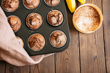 Homemade banana chocolate muffins sprinkled with sugar in a baking form on a wooden background. Top view.