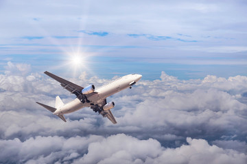 White commercial airplane flying away in to sky high altitude above the white clouds with sunlight travel destinations concept.