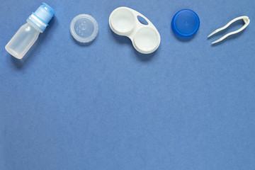 Accessories for contact lenses: a solution container, a pair of tweezers. Blue background.