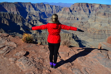 A tourist girl presents herself as a bird flying over the canyon and Colorado river  in Grand Canyon West Park, Arizona, USA