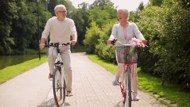 happy senior couple riding bicycles at summer park