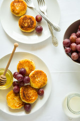Breakfast with mini cheesecakes, grapes, cream and honey on a white plate