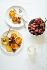 Breakfast with mini cheesecakes, grapes, cream and honey on a white plate