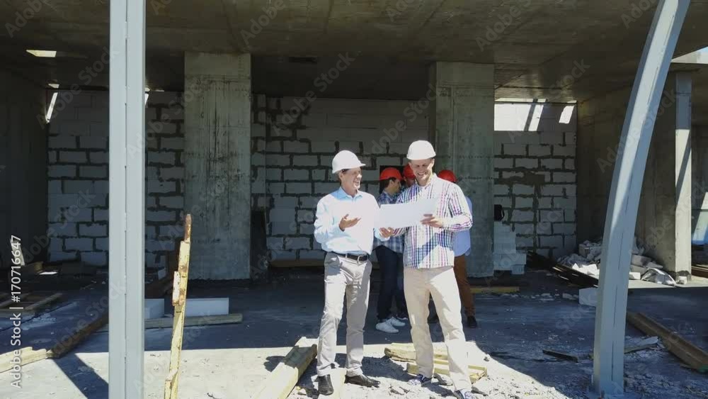 Poster aerial shot of builders team on construction site discussing plan of project with architect and cont