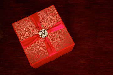 Red gift box with Chinese pin ornament for Happiness on top of a ribbon.
