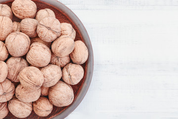 whole walnuts in a clay plate on a white wooden background. Rustic style.