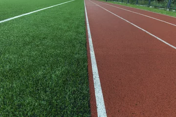 Gordijnen Running track and green grass field stadium © Ma